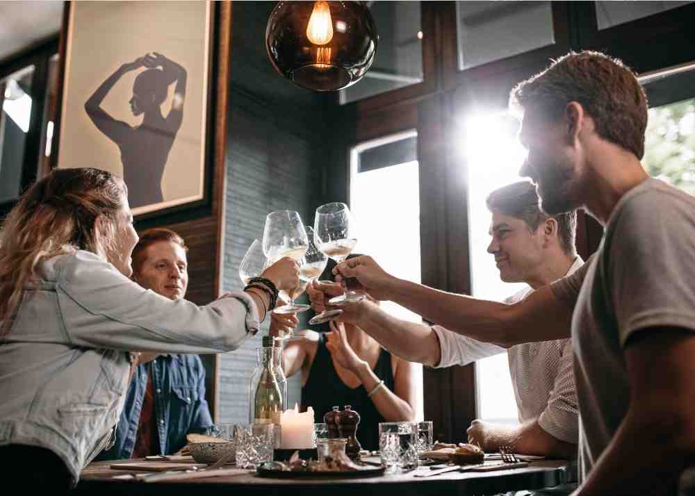 A group of 5 friends all cheering their wine glasses at a restaurant.